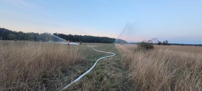 Bild vergrößern: Drei Personen stehen mit Wasserschluchen auf einem Feld und lschen.