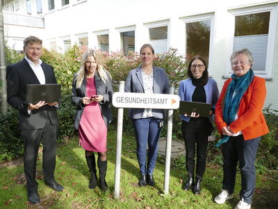 Bild vergrößern: Ein Gruppe von 5 Personen steht vor einem Gebude und blickt lchelnd in die Kamera. Im Vordergrund ist ein Schild mit der Aufschrift "Gesundheitsamt" zu sehen.