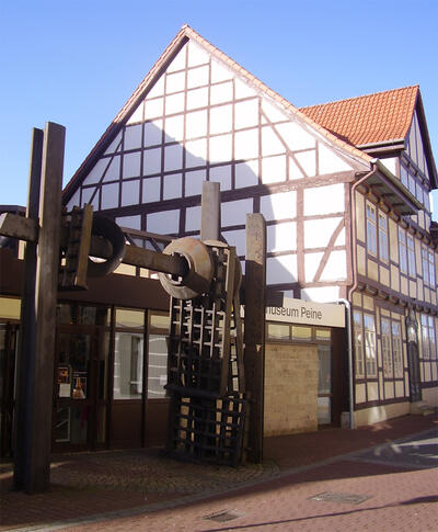 Bild vergrößern: Auf dem Foto ist der Eingang zum Kreismuseum Peine zu sehen mit einer groen Eisenskulptur davor und einem Fachwerkhaus im Hintergrund.