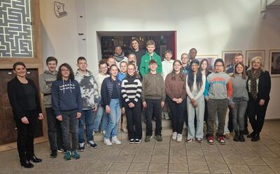 Bild vergrößern: Eine Gruppe von Jungen und Mdchen steht versetzt voneinander vor Stufen in einem Gebude, flankiert von vier Erwachsenen.