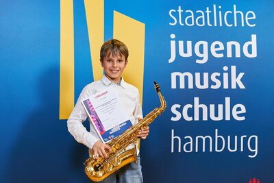 Bild vergrößern: Ein junger Mann hlt sein Saxophon und eine Urkunde in den Hnden und lchelt in die Kamera.