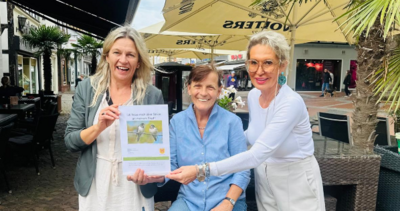 Bild vergrößern: Drei Frauen stehen drauen vor einem Stehtisch und halten gemeinsam einen Aufsteller in den Hnden.