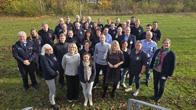 Bild vergrößern: Eine Gruppe von Frauen und Mnnern steht im Kreis auf einer Rasenflche und blickt in die Kamera.