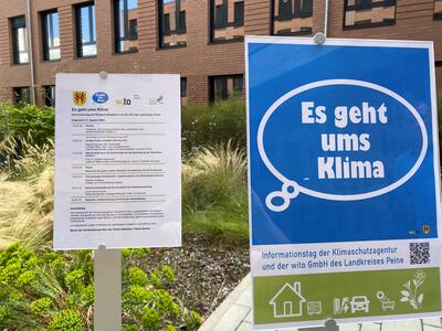 Bild vergrößern: Auf der linken Seite des Fotos ist ein Zettel mit einem Programm zu sehen, rechts danebem ein Poster mit der Aufschrift "Es geht ums Klima". Im Hintergrund sind Planzen und ein Gebude