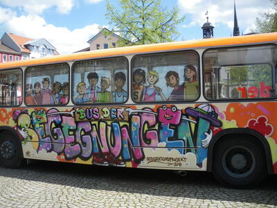 Bild vergrößern: Es ist der mittlere Teil eines bunt bemalten Busses zu sehen, auf dem das Wort "Begegnungen" geschrieben steht.