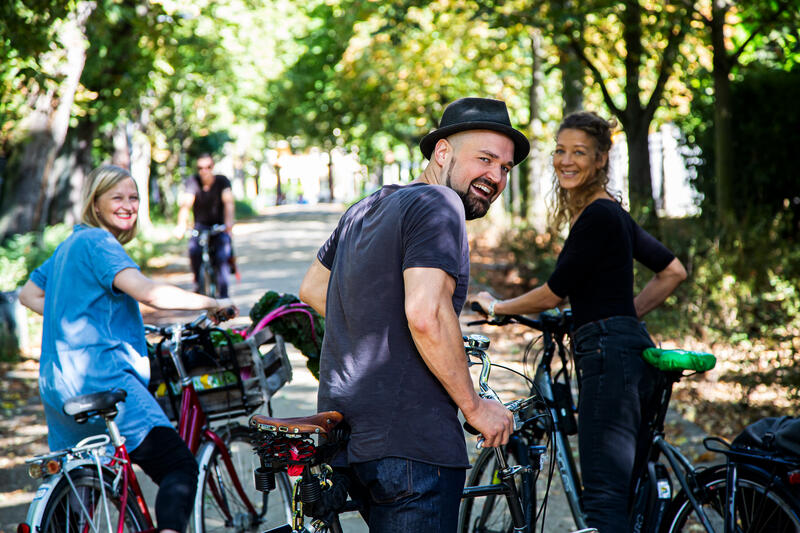 Zwei Frauen und ein Mann sind dabei, auf ihre Fahrräder zu steigen. Kurz vorher blicken sie sich noch einmal lächelnd zu dem Fotografen um.