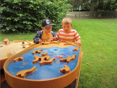 Bild vergrößern: Zwei kleine Jungen stehen auf einer grnen Wiese an einem Spieltisch fr Murmeln.