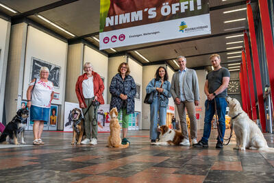 Bild vergrößern: In einer Bahnhofshalle stehen vier Frauen und zwei Mnner mit fnf Hunden nebeneinander. Alle blicken lchelnd in die Kamera.