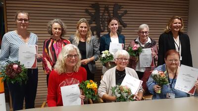 Bild vergrößern: Auf dem Bild sind 9 Frauen zu sehen, drei von ihnen sitzen im Vordergrund an einem Tisch, sechs stehen hinter ihnen vor einer holzvertfelten Wand mit dem Wappen des Landkreises Peine. Einige der Frauen halten Urkunden und Blumenstrue in den Hnden.