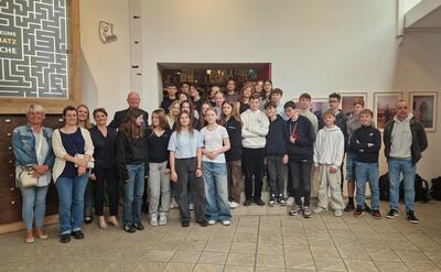 Bild vergr&ouml;&szlig;ern: Eine Gruppe von M�dchen und Jungen steht versetzt zueinander in einem gro�en Raum. An beiden Seiten stehen zudem Erwachsene. Alle l�cheln in die Kamera.