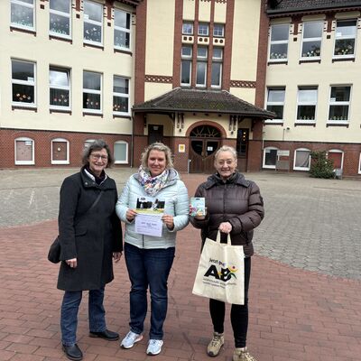 Bild vergrößern: Drei Frauen stehen auf dem Schulhof vor einem Schulgebude. Die Frau ganz rechts hlt eine Stofftasche, die Frau in der Mitte eine Urkunde in der Hand.