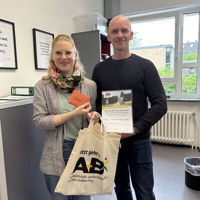 Bild vergrößern: Eine Frau und ein Mann stehen in einem Bro und lcheln in die Kamera. Die Frau halt eine Stofftasche und einen Zettel mit der Aufschrift "Danke!" in den Hnden, der Mann hlt eine Urkunde in der Hand.