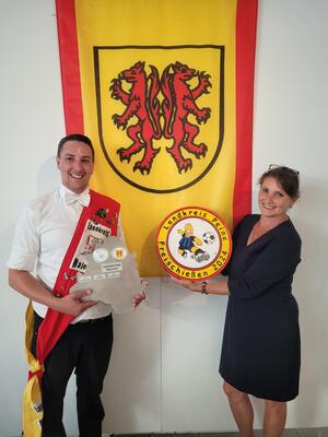 Bild vergrößern: Eine Frau und ein Mann stehen vor einer weien Wand, die das Kreiswappen zeigt.