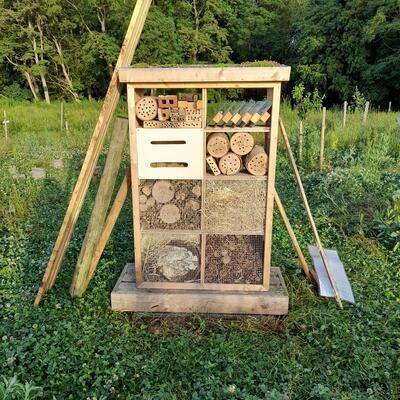 Bild vergr&ouml;&szlig;ern: Das Foto zeigt ein Insektenhotel aus Holz, das auf einer gr�nen Wiese steht. Im Hintergrund ist Baumbestand zu sehen.