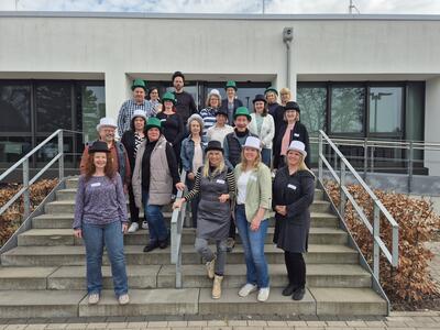 Bild vergrößern: Eine Gruppe von Menschen steht vor einem Gebude auf einer Treppe. Fast alle tragen Zylinder in verschiedenen Farben.
