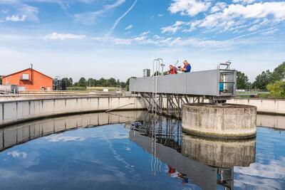 Bild vergrößern: Zwei Mnner stehen auf einer Metallbrcke ber einem runden Becken, das mit Wasser gefllt ist.