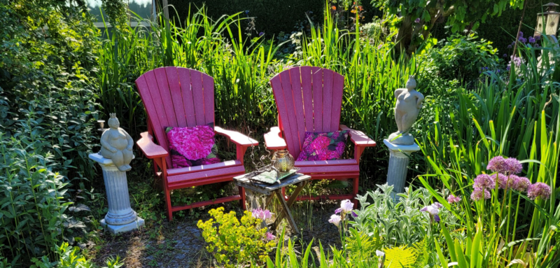 Zwei pinkfarbene Holzstühle mit Lehne stehen in einer grünen Gartenoase.