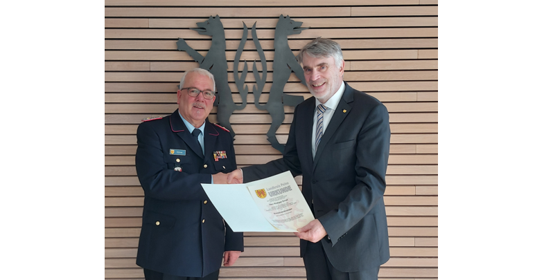 Zwei M&auml;nner stehen vor einer vert&auml;felten Wand, die das Kreiswappen in schwarz zeigt. Sie geben sich die Hand und l&auml;cheln in die Kamera.