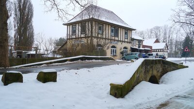 Bild vergr&ouml;&szlig;ern: Das Foto zeigt ein altes Fachwerkgeb�ude schr�g von vorne in einer Schneelandschaft. Im Vordergrund ist eine kleine Br�cke zu erkennen.