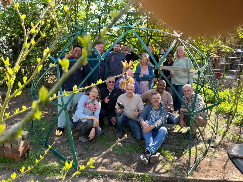 Eine Gruppe von Frauen und M&auml;nnern sitzt und steht versetzt zueinander in einem Garten.