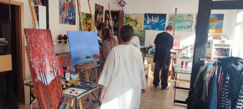 Einige Jugendliche stehen in einem Atelier vor Staffeleien und gestalten ihr Werk.