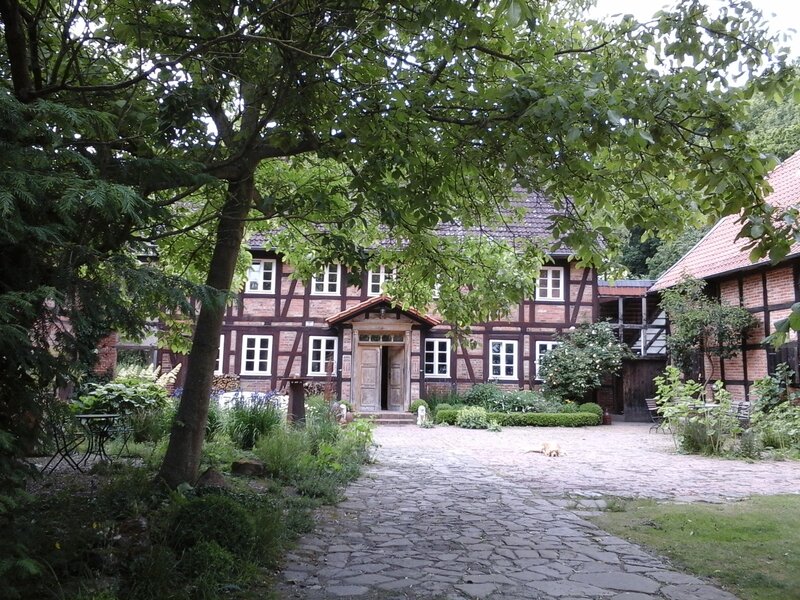 Ein geplasteter Weg f&uuml;hrt zu einem gro&szlig;en Fachwerkhaus. Rings herum bl&uuml;ht und gr&uuml;nt es.