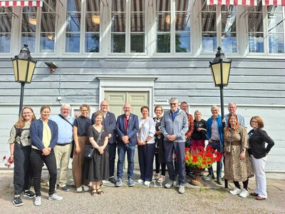 Bild vergr&ouml;&szlig;ern: Eine Gruppe von Frauen und M�nnern steht vor dem Eingang eines Hauses und l�chelt in die Kamera.